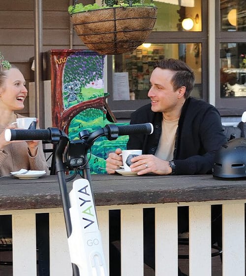 young couple drinking coffee at Brisbane cafe after riding VAYA Go Electric Scooters